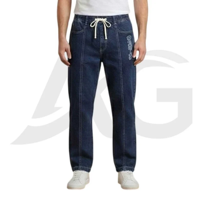 Front view of men's dark blue baggy denim joggers featuring an elastic waist, white drawstring, vertical front leg seams, and a graphic detail on the left thigh, paired with white sneakers.