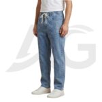 Side profile view of men's light blue baggy denim joggers demonstrating the loose streetwear fit, front seam, and graphic detail.