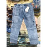 Back view of light blue denim cargo pants held up in a retail setting, highlighting the gathered elastic waist, rear pockets with tags, and side cargo pockets.
